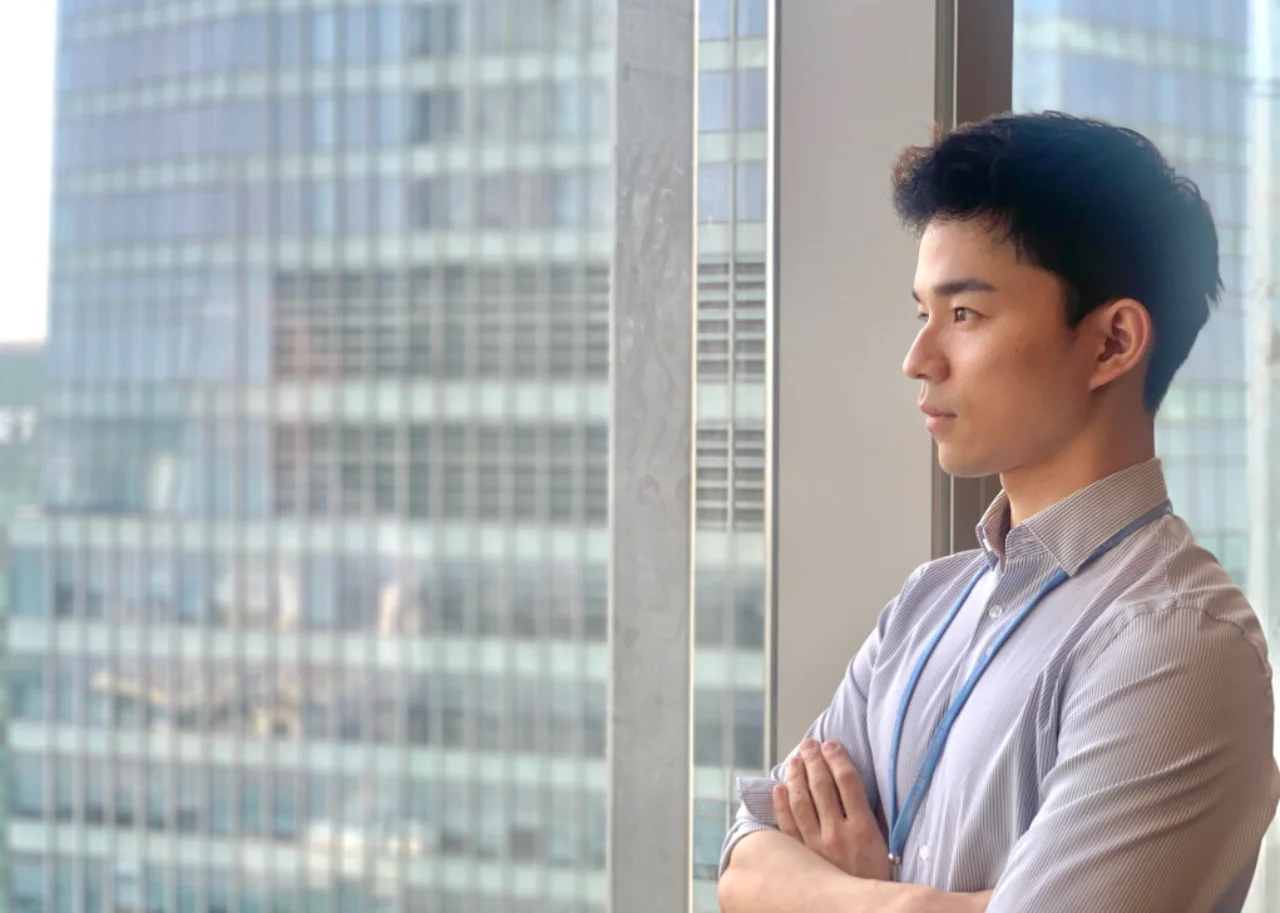 Sean steht vor einem Fenster in einem Deutsche Bank Hochhaus